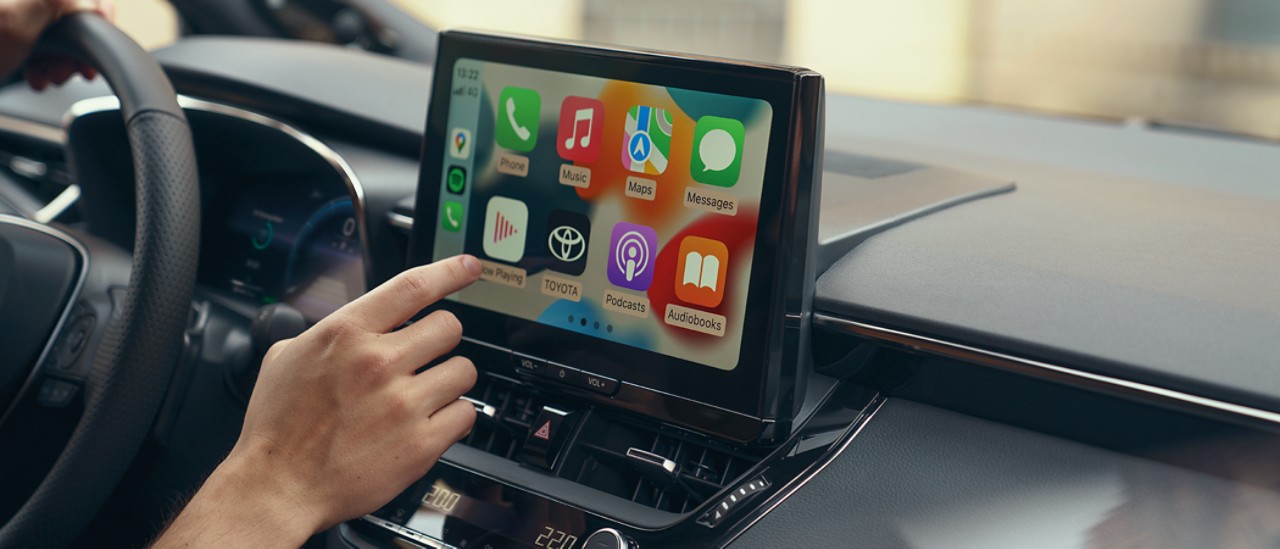Osoba vo vozidle Toyota používa multimediálnu dotykovou obrazovkou vozidla a na displeji sa zobrazuje domovská obrazovka Apple CarPlay.